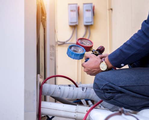 A technician in a blue shirt checks pressure gauges on HVAC equipment, with connecting hoses visible in a well-lit outdoor setting.